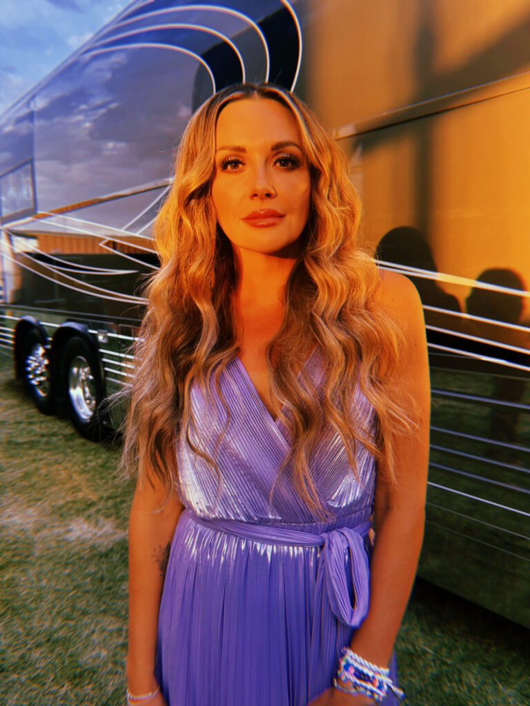 Carly Pearce standing beside tour bus wearing purple dress