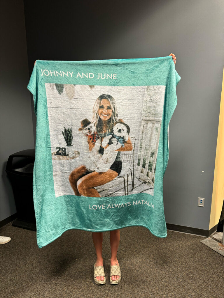 Carly Pearce holding up a blanket featuring a photo of her holding dogs johnny and june