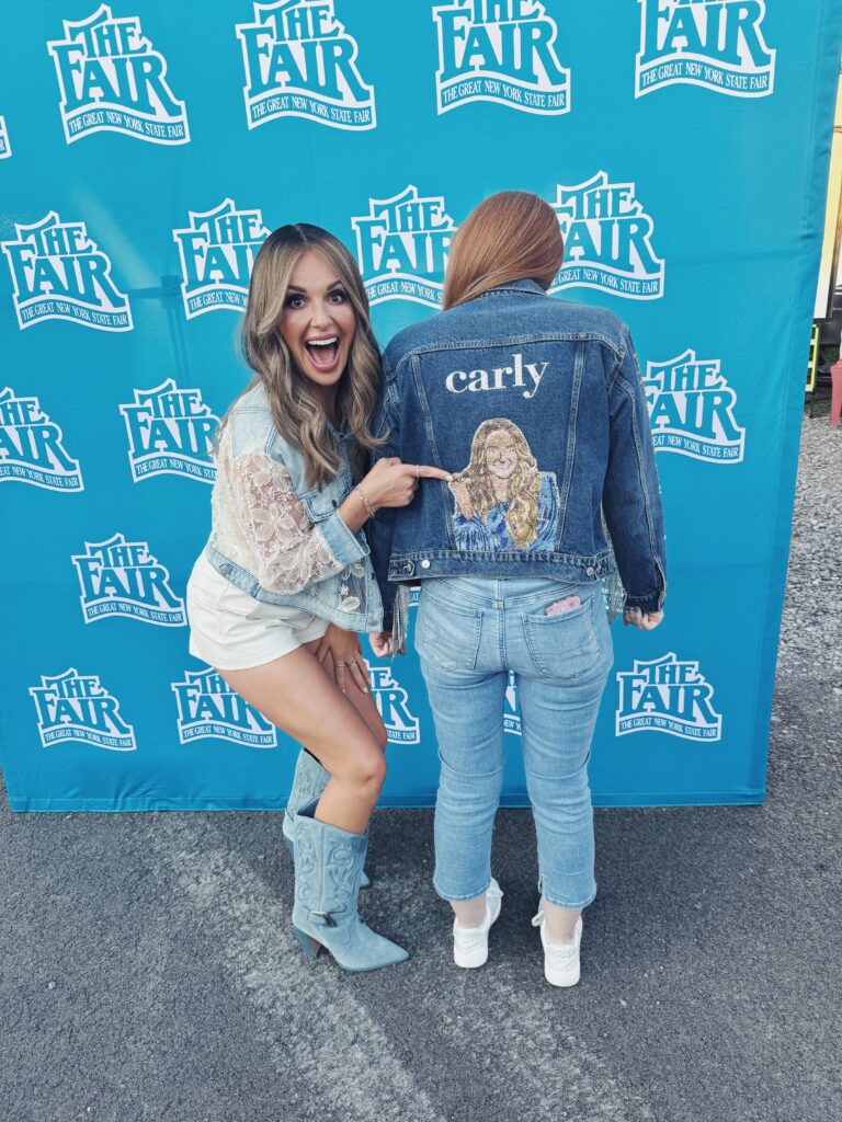 Carly posing with a fan wearing a jacket with her picture on the back